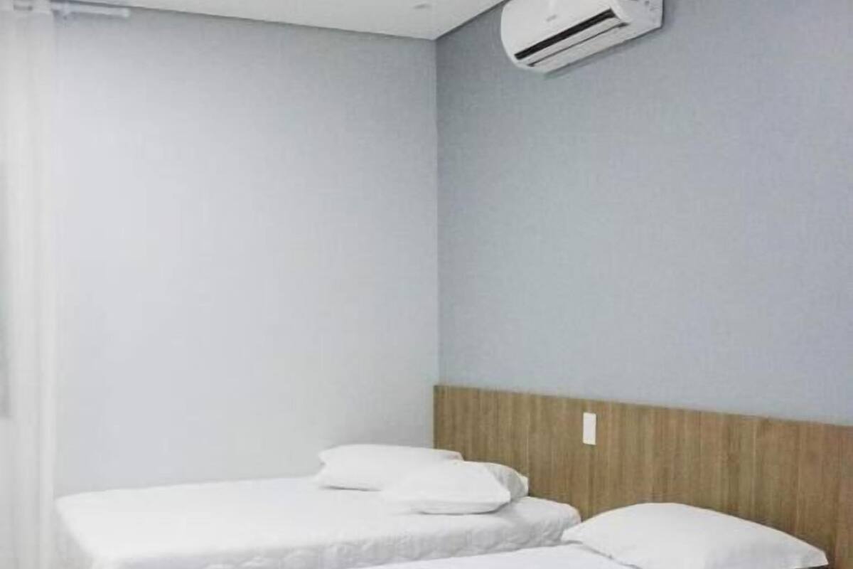 A room with two beds, a wooden headboard, a white air conditioning unit, and a wooden floor.