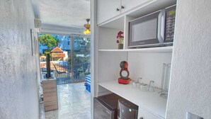 Een compacte keuken met een magnetron, een koffieapparaat en een kleine koelkast. Er is een glazen deur naar een buitenruimte met een tafel en stoelen.