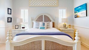 Une chambre à coucher avec un lit blanc, deux tables de chevet, une tête de lit en osier et un panneau décoratif au plafond.