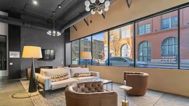 A modern interior with a sofa, armchairs, a coffee table, a lamp, and a large window with a view of buildings and cars.