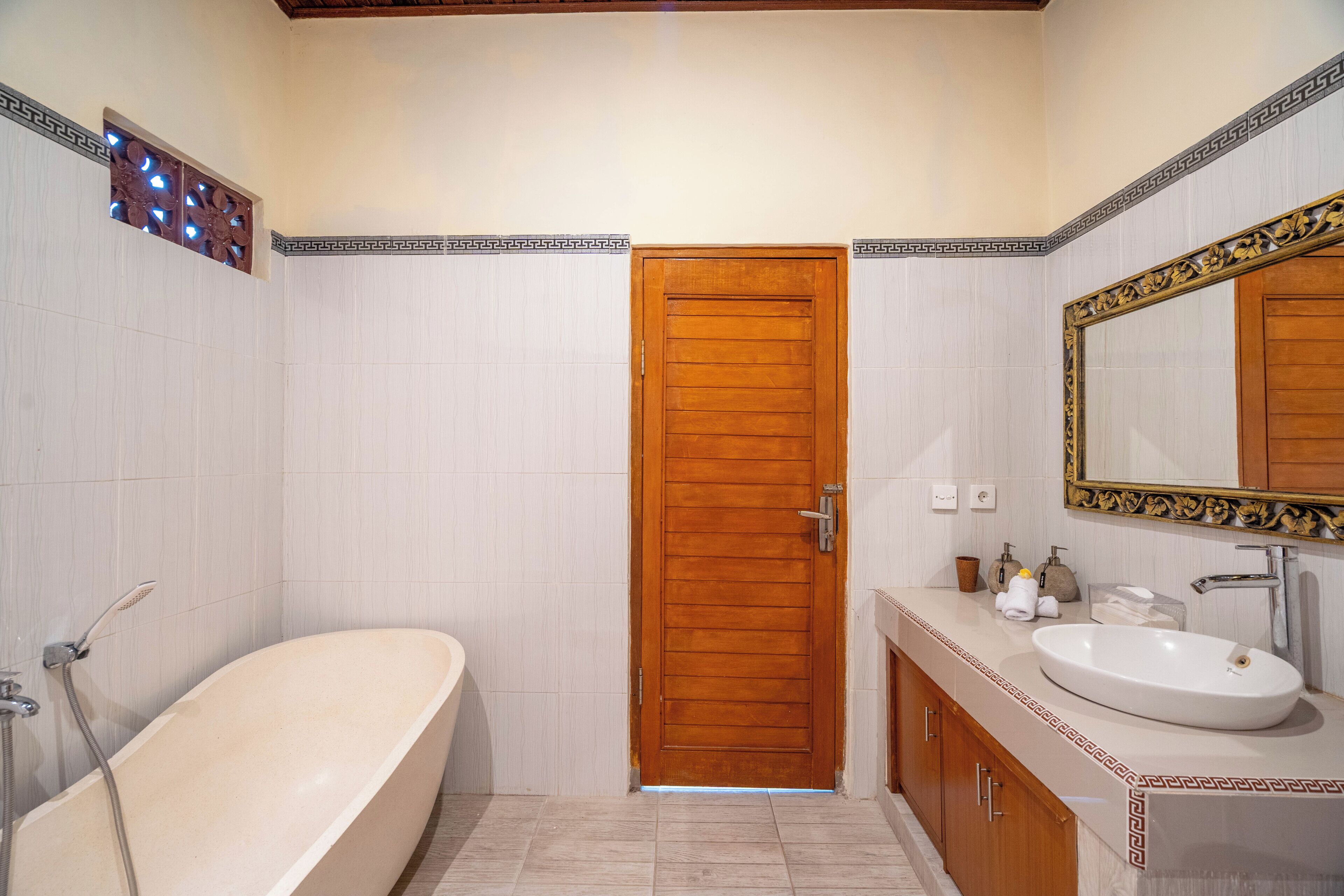 A bathroom with a wooden door, a bathtub, a sink, and a mirror with an ornate frame.