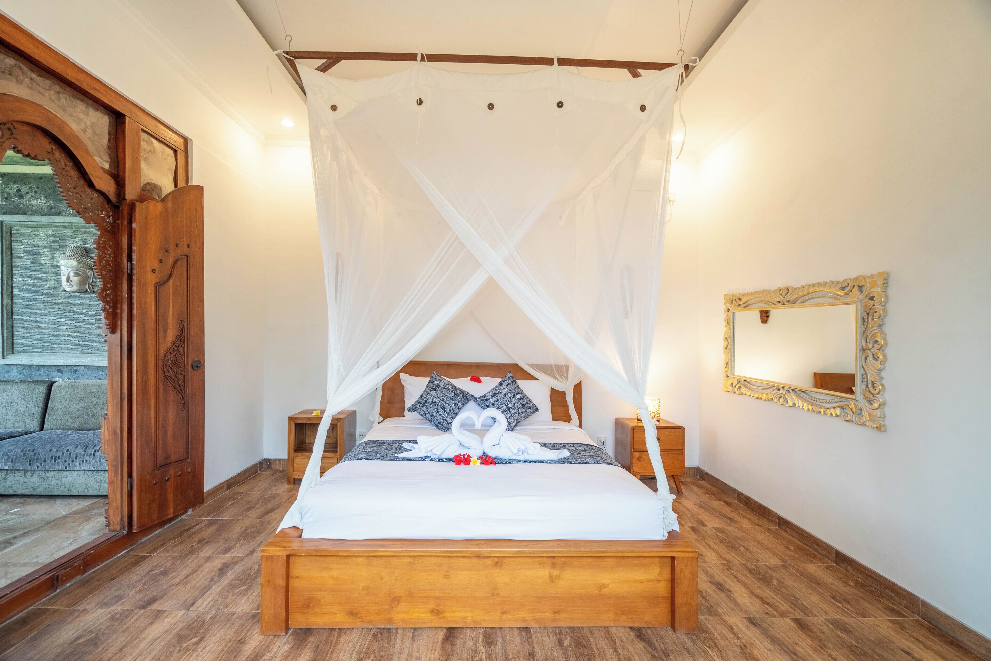 Un lit à baldaquin, une tête de lit en bois, une table de chevet, un miroir et un mur en pierre.