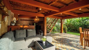 A covered outdoor seating area with a sofa, a table with a plant, and a wooden bench. - Aris Villa Ubud (Ubud)