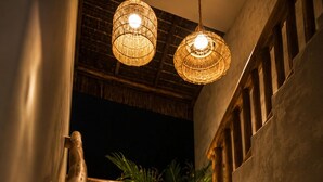Un escalier en bois avec une rampe, deux lampes en osier suspendues et une vue sur la verdure à l’extérieur.