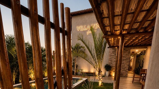 Une terrasse en bois avec une piscine, un espace couvert doté d’un toit de chaume et une enseigne indiquant « Villa ».