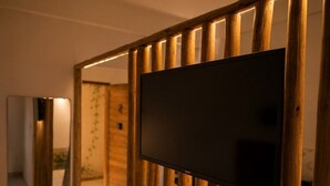 Un intérieur moderne avec une cloison en bois, un téléviseur à écran plat fixé sur celle-ci et un miroir qui reflète une partie de la pièce.