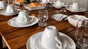 Une table dressée pour un repas, avec de la vaisselle blanche et des verres, une plante en arrière-plan et un mur à la surface texturée.
