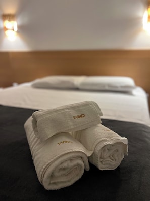 A neatly made bed with white linens and a folded towel with 'VINC' embroidered on it. - Villa Vinci Flat (São Miguel do Gostoso)