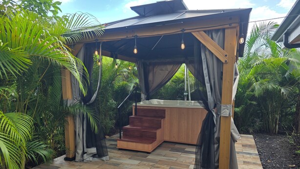 Un pabellón de madera con un jacuzzi, rodeado de exuberante vegetación.