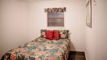 A bedroom with a floral bedspread, a window with blinds, and a framed picture on the wall.