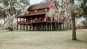 A wooden house with a porch, surrounded by trees. - Riverfront, HotTub, BoatRamp, Deck, Sleeps 24 (West Columbia)