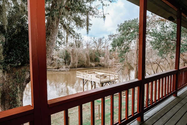 A wooden deck overlooking a river with a dock and surrounding vegetation.