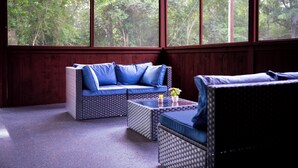 A room with a large window, wicker furniture, and a view of trees.