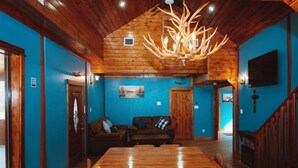 A spacious room with a wooden ceiling, a dining table, and a large chandelier.