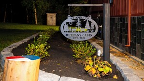A welcome sign for the Bethany Cabin, established in 2025, with a garden pathway leading to a wooden cabin.