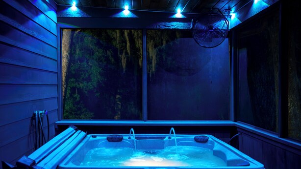 A hot tub with a control panel, surrounded by wooden walls and a window with a view of trees.