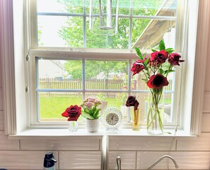 Una ventana con vistas a un jardín verde, un reloj y varios jarrones con flores.