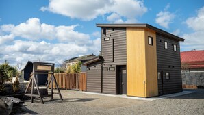 Ein modernes, zweistöckiges Gebäude mit Holz- und Grauverkleidung, einer Schaukel und einem umzäunten Garten.