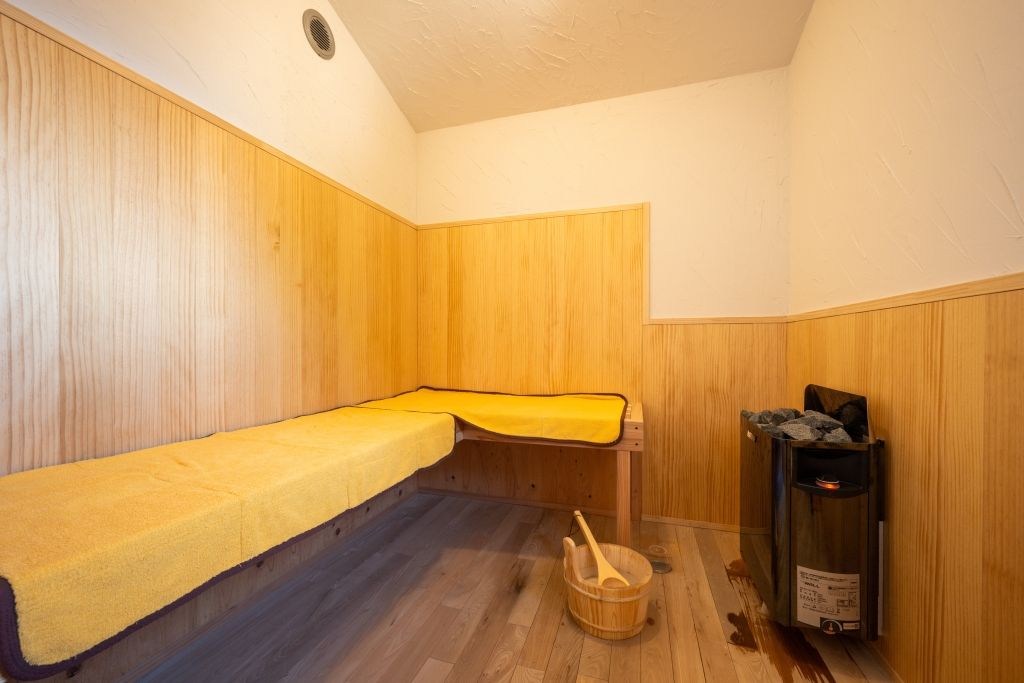 A sauna room with a bench, a wooden bucket, and a heater.