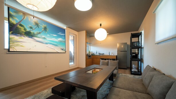 Ein modernes Wohnzimmer mit einem Holzesstisch, einem grauen Sofa und einem großen Gemälde zum Thema Strand an der Wand.