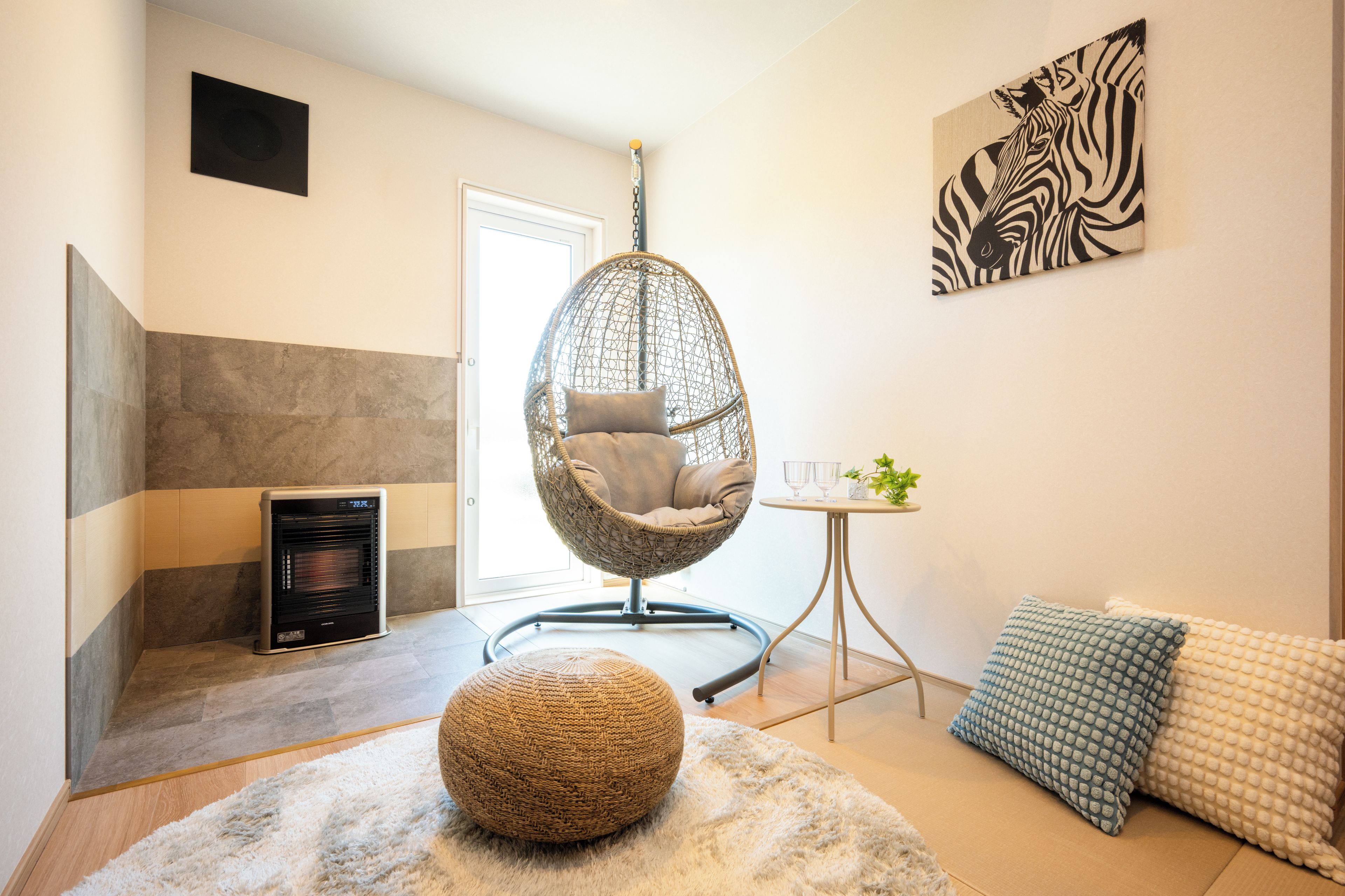 A modern living room with a hanging chair, a small table with a plant, and a zebra artwork on the wall.