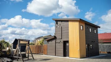 A modern two-story building with a wooden and grey facade, a swing set, and a fenced yard.