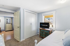 A hotel room with a bed, a television, a dresser, and a window with a view of a building. - Charming 1BR Beach Retreat on Wesley Ave (Ocean City)