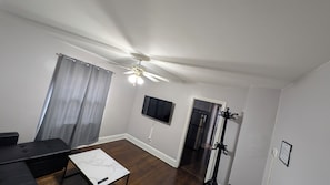 Ein modernes Wohnzimmer mit Deckenventilator, Flachbildfernseher, schwarzem Sofa und Esstisch.