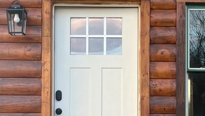 Puerta blanca con un pequeño ventanal sobre ella, en una cabaña de troncos de madera.