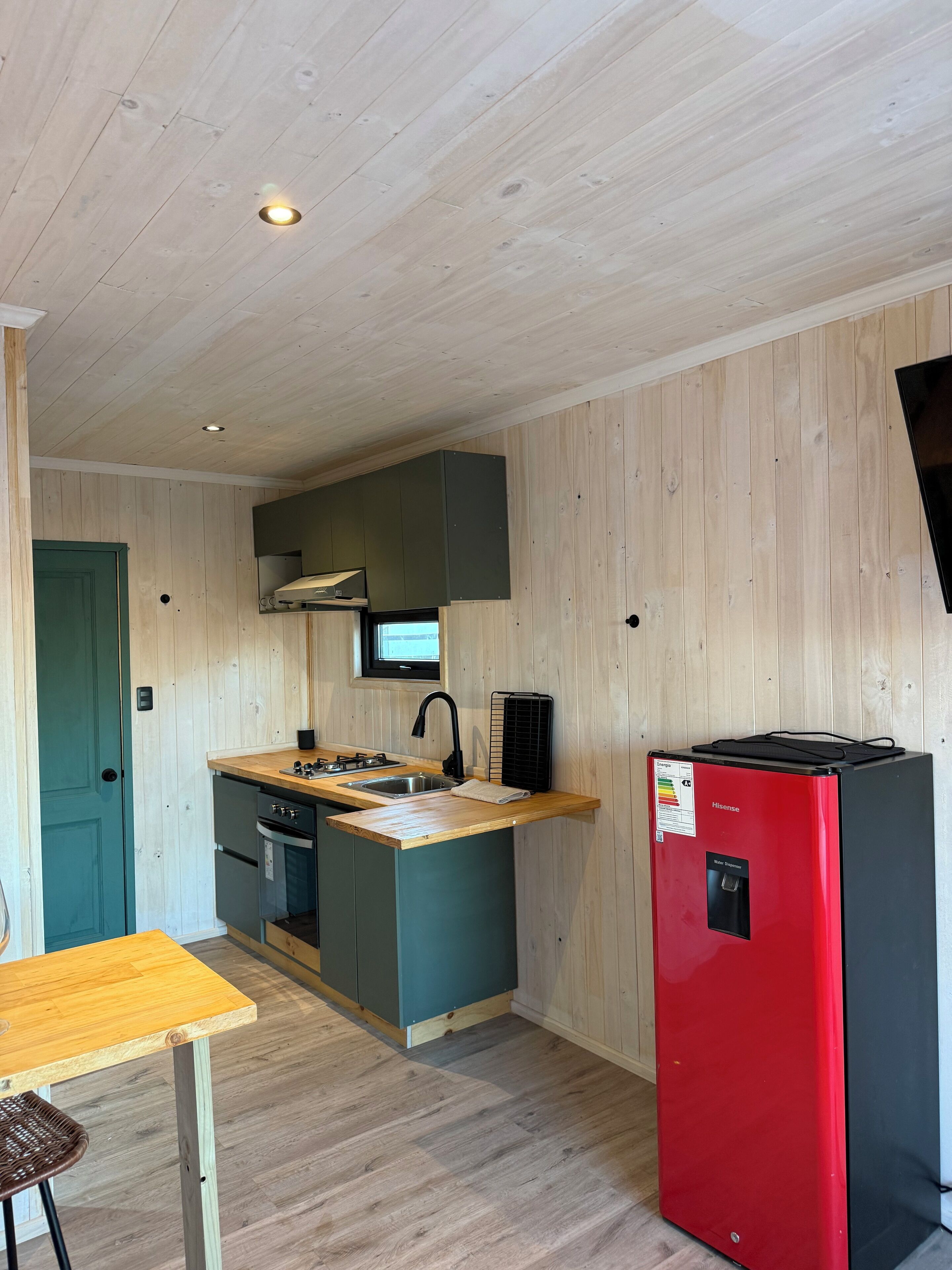Eine kleine Küche mit Holzwänden, einem Spülbecken, einem Herd und einem roten Kühlschrank.