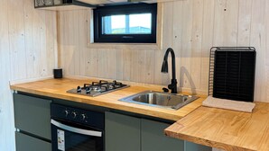 Een kleine keuken met een houten aanrecht, een inbouwoven, een spoelbak en een raam boven de spoelbak.