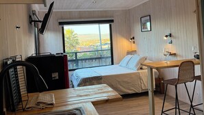 Een gezellige kamer met een bed, een houten bureau, een stoel, een wastafel en een groot raam met uitzicht op de omgeving.