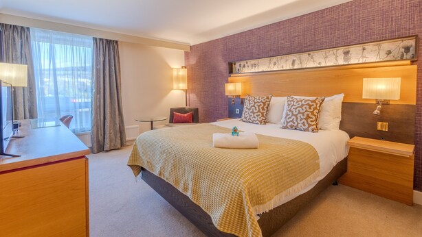 Ein Hotelzimmer mit einem großen Bett, Nachttischlampen, einem Schreibtisch und Blick ins Freie.