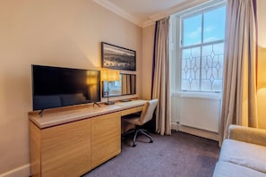 A hotel room with a wooden desk, a flat-screen TV, a chair, a window with curtains, and a radiator. - Doubletree by Hilton Dunblane Hydro (Dunblane)