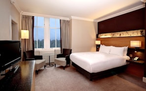 A hotel room with a bed, a TV, a desk, two chairs, a window with curtains, and a headboard with a floral design. - Doubletree by Hilton Dunblane Hydro (Dunblane)
