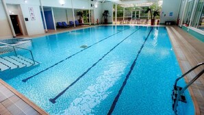 Ein Hallenbad mit deutlich markierten Bahnen, einem Sprungbrett und Liegestühlen.