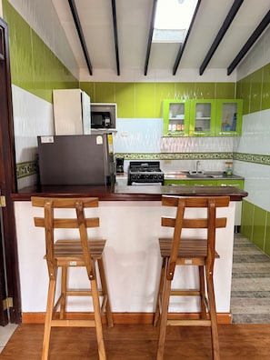 Una cocina con baldosas verdes y blancas, un microondas, una estufa y dos taburetes de madera para bar.
