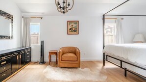 Un dormitorio con cama con dosel, un calentador portátil, un sillón de cuero, un cuadro enmarcado en la pared y un espejo grande.