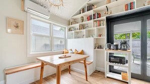 Una cocina acogedora con una mesa de madera, estantes blancos con libros y utensilios de cocina, y vistas al exterior.