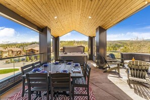 A spacious outdoor dining area with a wooden ceiling, a large table set for four, and a view of a mountainous landscape. - VIP Concert Viewing from Private Hot Tub+Walkable+5BR+Sauna+Kids Ski Gear Free (Winter Park)