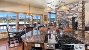 A kitchen with a stone fireplace, large windows, and a dining area with chairs and a table. - Alpine Lakes Lodge, 3bd Ensuites+35 Acres+Dogs+Kids+Sleeps8+Air Conditioning! (Archuleta County)