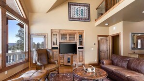 A spacious living room with a large TV, leather furniture, and a view of the outdoors. - Alpine Lakes Lodge, 3bd Ensuites+35 Acres+Dogs+Kids+Sleeps8+Air Conditioning! (Archuleta County)