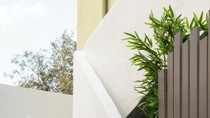 A set of stairs leading up to a building with a modern design, a white wall, and a wooden fence with greenery behind it. - Basil Leaf - Minimal View Retreat (Gonia)