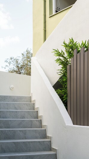 Eine Treppe führt zu einem Gebäude mit modernem Design, einer weißen Wand und einem Zaun mit Grünpflanzen.