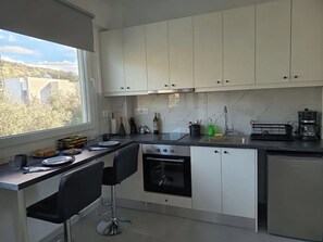 Eine moderne Küche mit weißen Schränken, einer schwarzen Arbeitsplatte, einem eingebauten Backofen und einem Fenster mit Blick auf Gebäude und Bäume.