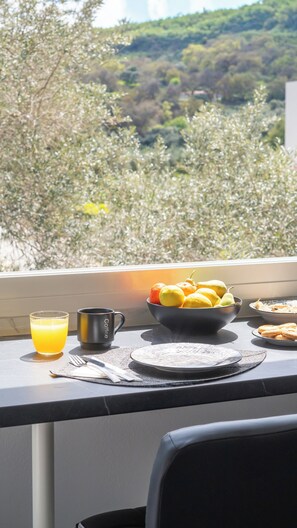 A breakfast table with a bowl of fruit, a glass of orange juice, and a coffee maker.