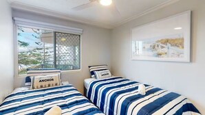 Ein Schlafzimmer mit zwei Betten, jeweils mit gestreifter Bettwäsche und Kissen mit dem Aufdruck 'ANCHOR'.