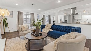 En moderne stue med en blå sofa, beige lænestole og et rundt sofabord.