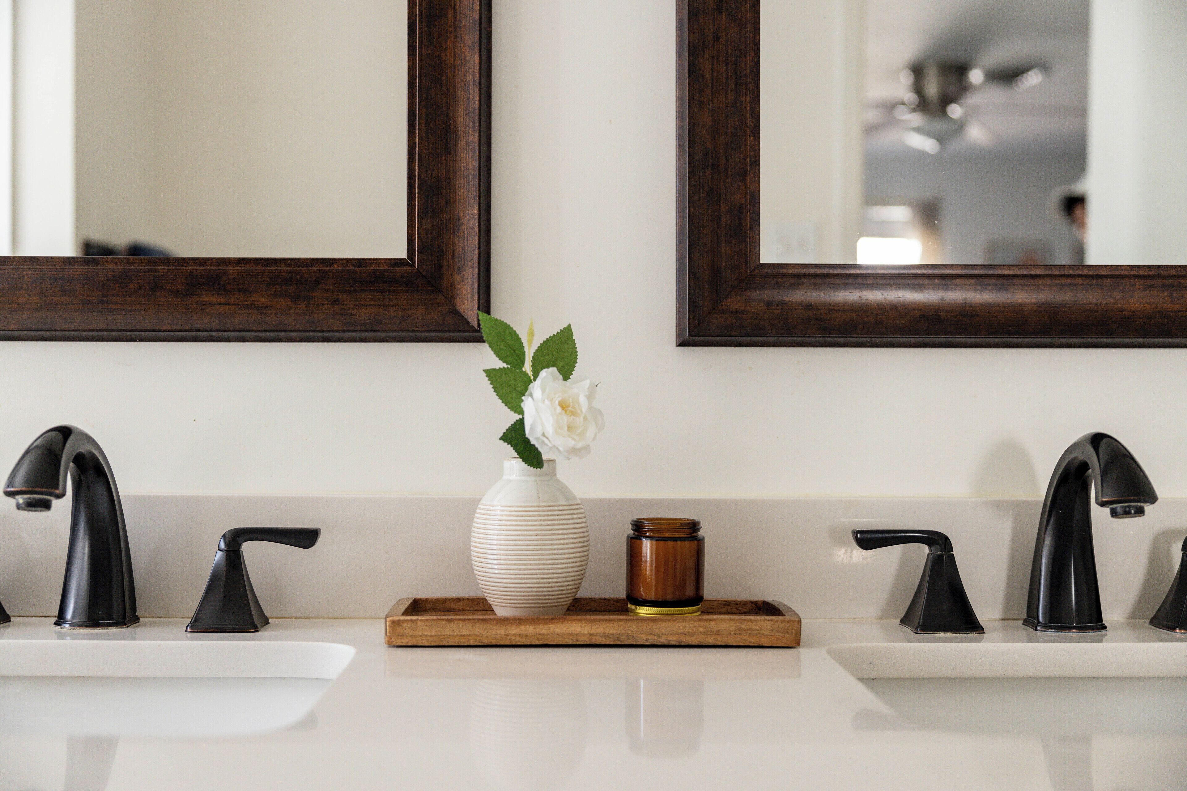 A bathroom with two sinks, a mirror, and a tray with a vase and candle.