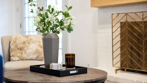 Et rundt træbord med en vase hvide blomster, et lys og en bakke med en bog og en lille æske.